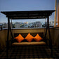 Swing with orange cushions in a room with a cityscape view at night.